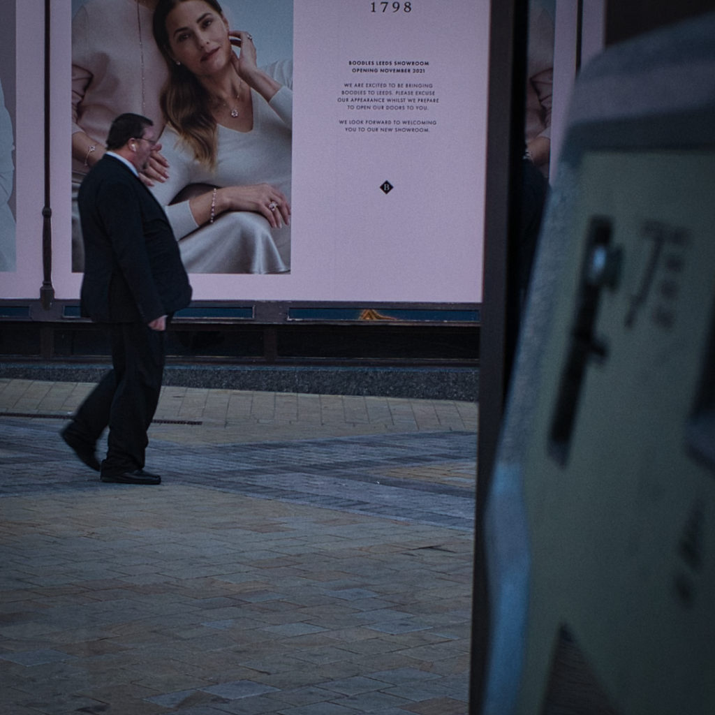 Street photography of man working past poster in Leeds