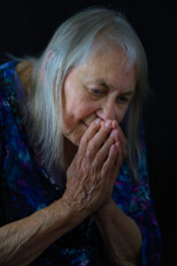 Older grey haired woman with hands together as if she is praying